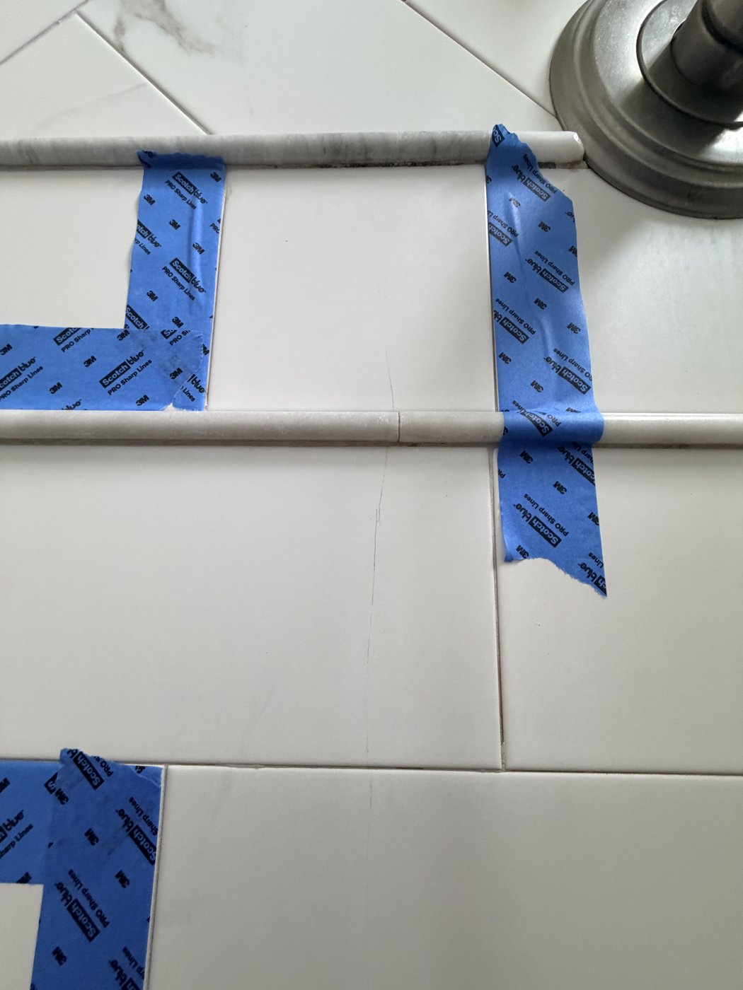 Cracked shower tiles marked for removal, cracks running through the tile and the marble pencil trim